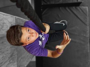A boy in purple shirt holding onto rope.